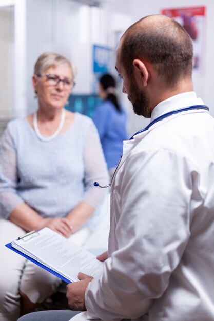 Docteur tenant un document médical tout en parlant avec une vieille femme âgée dans le cabinet de la clinique