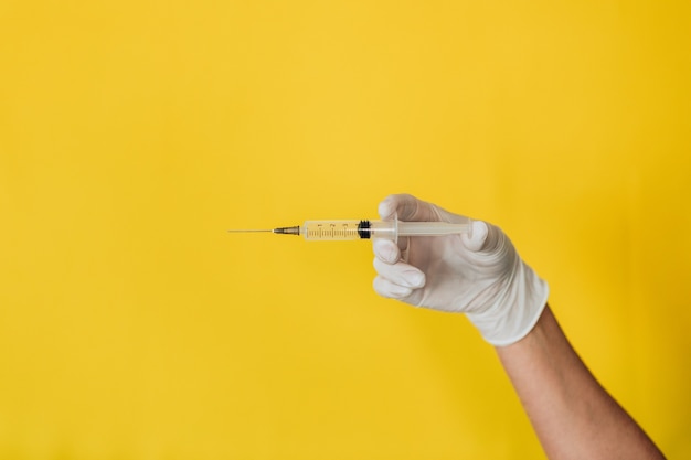 Docteur tenant une seringue sur un mur jaune