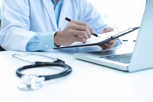 Docteur travaillant avec un ordinateur portable et écrit sur la paperasse. Contexte de l&#39;hôpital.