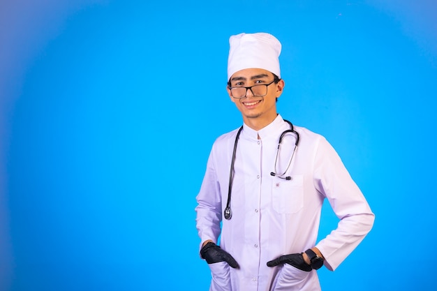 Docteur en uniforme médical blanc avec stéthoscope a mis ses mains dans sa poche et souriant.