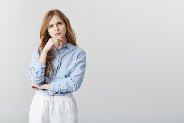 Dois-je vraiment aller en réunion. Portrait de jeune fille caucasienne sérieuse aux cheveux blonds, touchant le menton et fronçant les sourcils, regardant de côté tout en pensant ou en se rappelant des informations importantes