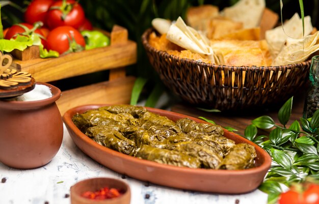 Dolma (tolma, sarma) - feuilles de vigne farcies avec du riz et de la viande. Sur la table de la cuisine avec du yaourt, du pain, des légumes. Cuisine traditionnelle du Caucase, Ottomane, Turque et Grecque