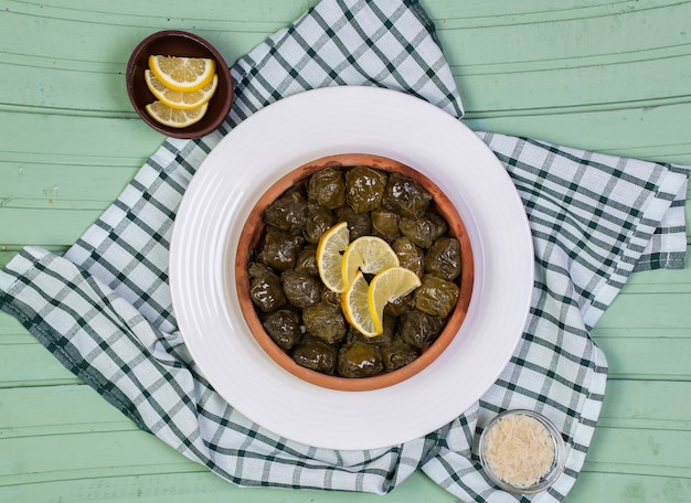 Dolmasi yarpag traditionnels avec des tranches de citron dans la plaque blanche sur une table verte.