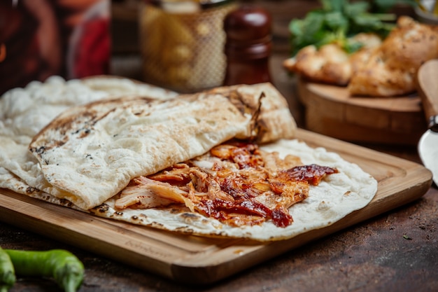 Photo gratuite doner kebab de poulet avec du ketchup à l'intérieur de pain plat sur planche de bois