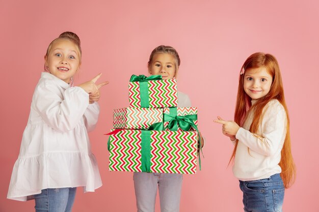 Donner et recevoir des cadeaux pendant les vacances de Noël. Groupe d'enfants souriants heureux s'amusant, célébrant isolé sur fond de studio rose. Rencontre du Nouvel An 2021, enfance, bonheur, émotions.