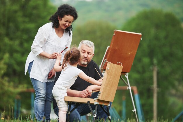 Donnez-moi ce pinceau. Grand-mère et grand-père s'amusent à l'extérieur avec leur petite-fille. Conception de peinture