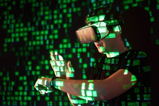 La double exposition d'un homme caucasien et d'un casque de réalité virtuelle vr est vraisemblablement un joueur ou un pirate informatique déchiffrant le code dans un réseau ou un serveur sécurisé, avec des lignes de code en vert