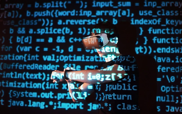 La double exposition d'un homme caucasien et d'un casque de réalité virtuelle VR est vraisemblablement un joueur ou un pirate informatique déchiffrant le code dans un réseau ou un serveur sécurisé, avec des lignes de code