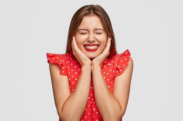 Douce belle femme avec rouge à lèvres posant contre le mur blanc