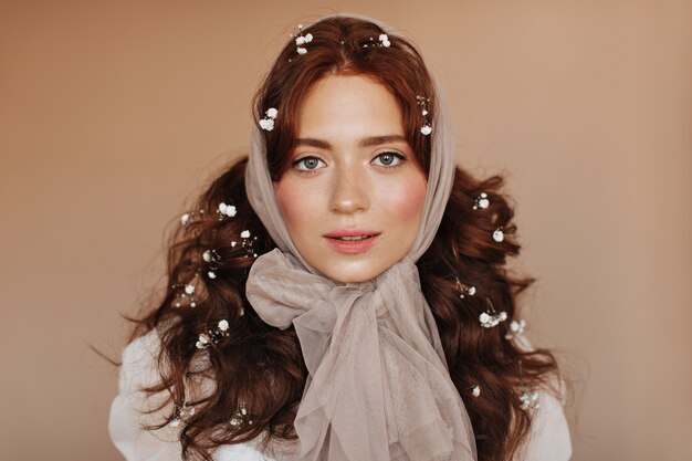 Douce dame avec des taches de rousseur et un fard à joues lumineux posant sur fond beige. Femme en casque souriant.