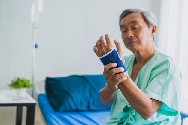 Douleur et douleur au poignet grand-père asiatique senior en uniforme de patient souffre du concept d'idées de santé de problème corporel