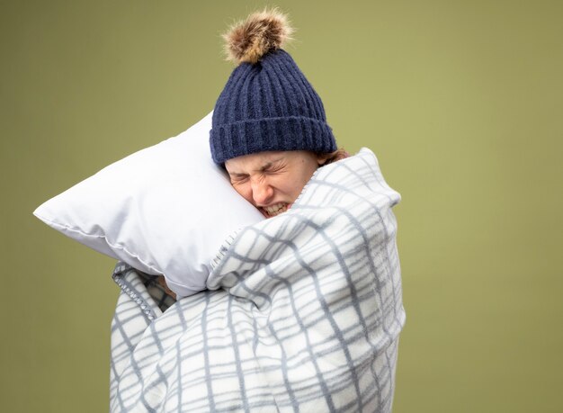 Douleur jeune fille malade portant robe blanche et chapeau d'hiver avec foulard enveloppé dans un oreiller étreint à carreaux