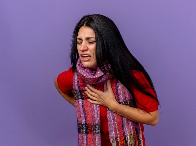 Douleur jeune fille malade de race blanche portant un foulard mettant les mains sur la poitrine et sur le dos avec les yeux fermés isolé sur le mur violet avec copie espace