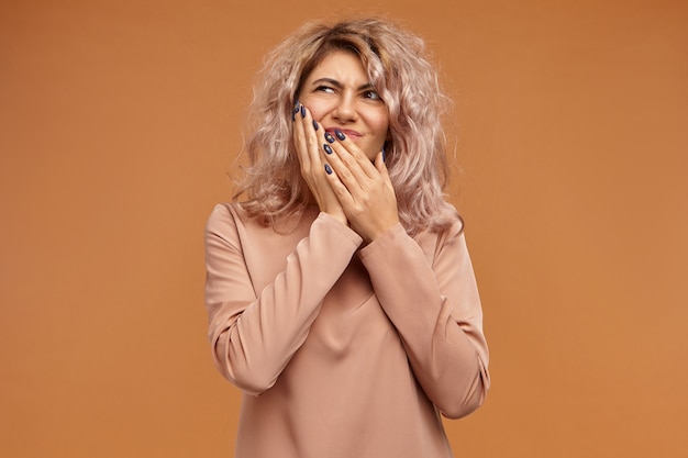 Douleur, maladie, santé, maladie, soins dentaires, personnes et concept de mode de vie. Émotionnelle frustrée jeune femme de race blanche avec une coiffure volumineuse mettant la main sur sa joue