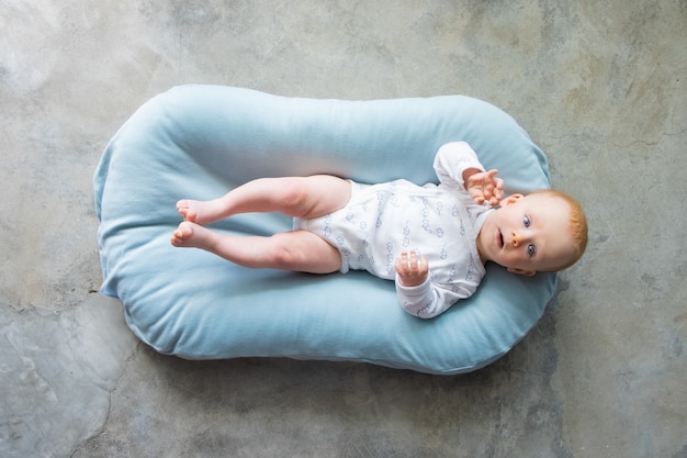 Doux bébé aux cheveux rouges allongé sur le dos dans un petit matelas