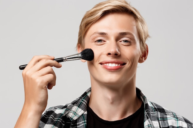 Drôle beau jeune homme blond portant une chemise à carreaux décontractée avec pinceau de maquillage