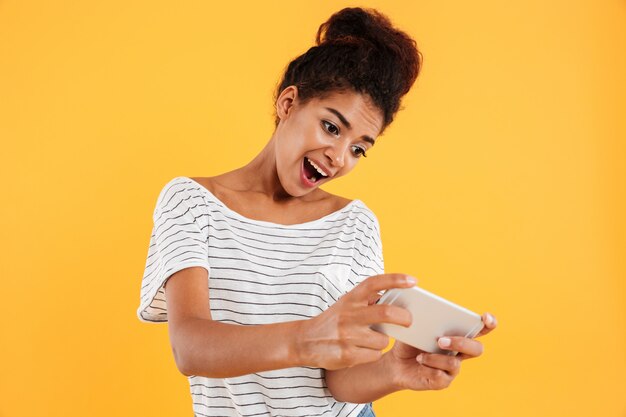 Drôle femme africaine positive jouant le jeu sur téléphone isolé