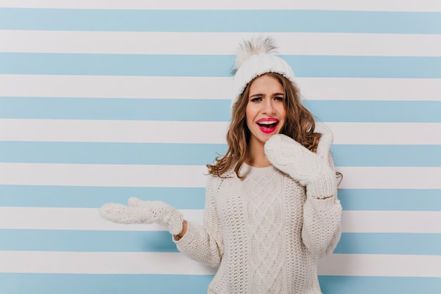 Photo gratuite drôle, fille au chapeau chaud et pull d'hiver fait le visage surpris. modèle slave pose pour portrait