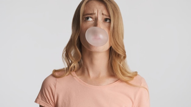 Photo gratuite drôle de fille blonde nerveuse soufflant du chewing-gum sur fond blanc bulles de bonbons