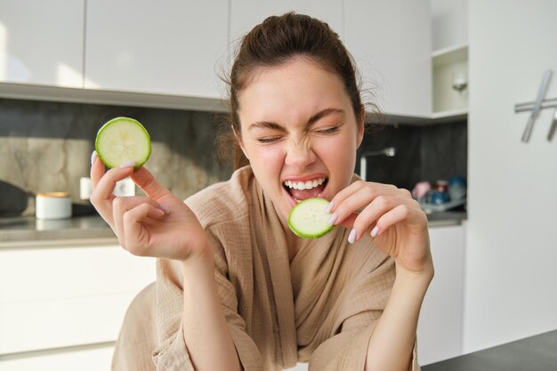 Photo gratuite drôle de fille heureuse mangeant sainement tenant des courgettes coupant des légumes pour un repas sain dans la cuisine