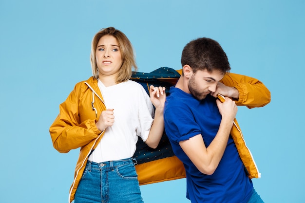 drôle jeune beau couple portant une veste sur le mur bleu