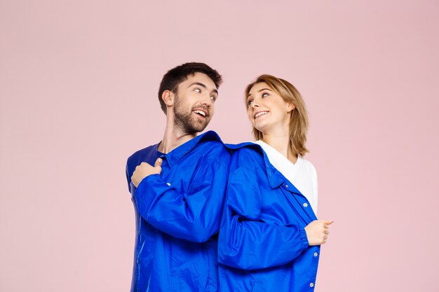 Drôle jeune beau couple portant une veste sur un mur rose clair