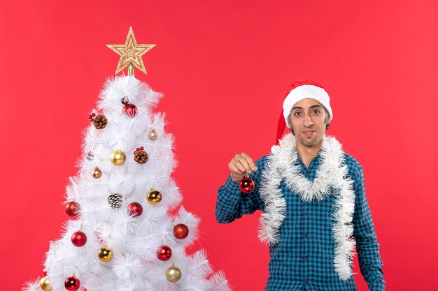 Drôle de jeune homme avec chapeau de père Noël dans une chemise dépouillé bleu et tenant l'accessoire de décoration