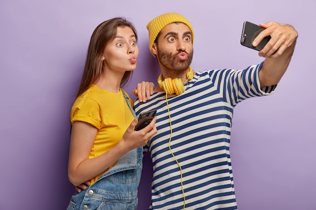 Drôle jeune homme et femme font la grimace, gardez les lèvres arrondies, prenez une photo sur la caméra avant du téléphone mobile moderne, prenez des photos de selfie