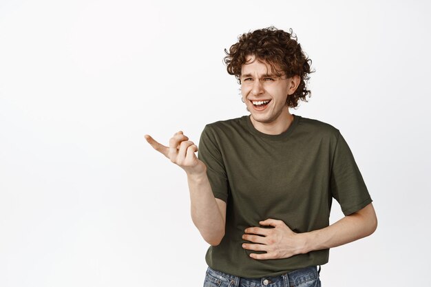 Drôle jeune homme riant pointant vers un petit rire hilarant et un sourire debout sur fond blanc