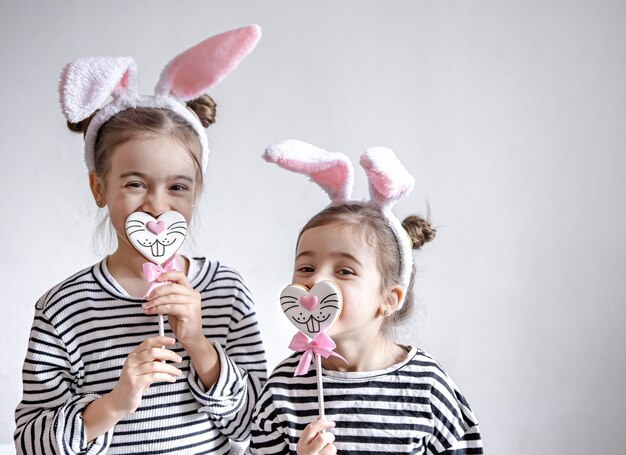Drôles de petites filles avec des oreilles de Pâques sur la tête et du pain d'épice de Pâques sur des bâtons.