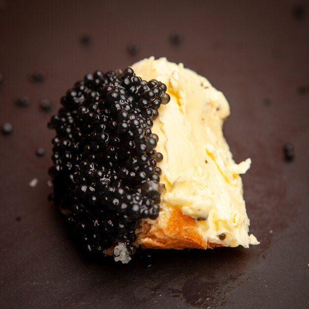 Du caviar noir avec du beurre sur du pain sur fond sombre, high angle view.