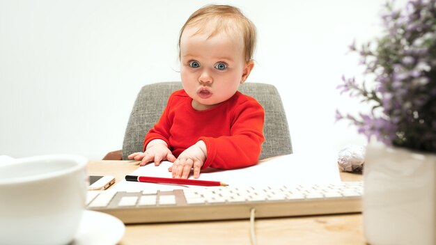 Dure journée. Enfant bébé fille assise avec clavier d'ordinateur moderne ou ordinateur portable en studio blanc