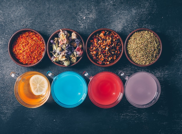 Photo gratuite l'eau colorée dans une tasse avec des herbes de thé dans des bols à plat sur un fond texturé sombre