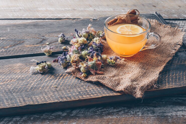 Photo gratuit l'eau de couleur orange dans une tasse avec des sortes de citron et de thé vue grand angle sur un tissu de sac et un fond en bois foncé