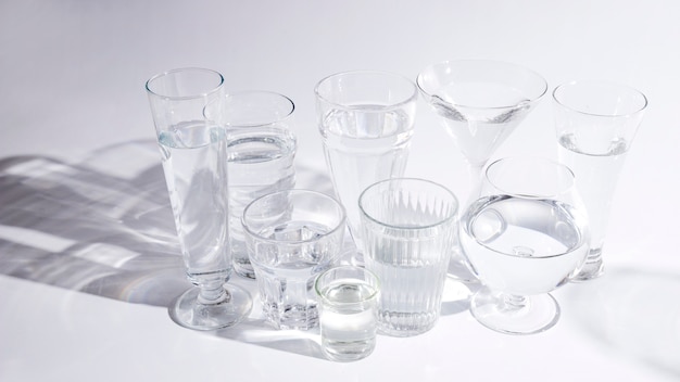 Eau dans différents types de verres avec une ombre sur fond blanc