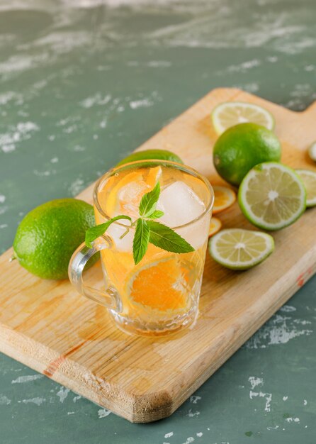Eau de désintoxication glacée avec orange, limes, menthe, planche à découper dans une tasse sur plâtre, high angle view.