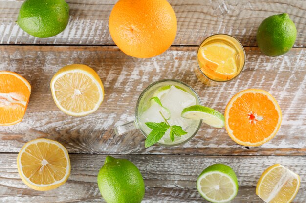 Eau détox avec limes, citrons, oranges, menthe en tasse et verre sur une surface en bois, mise à plat.