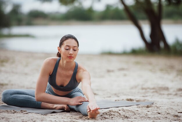 Echauffement facile. Brunette avec une belle forme de corps dans des vêtements sportifs ont une journée de remise en forme sur une plage