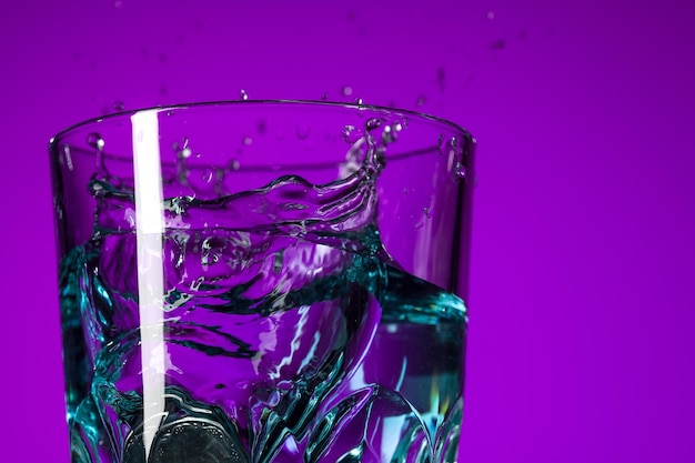 Les éclaboussures d'eau dans le verre sur fond lilas