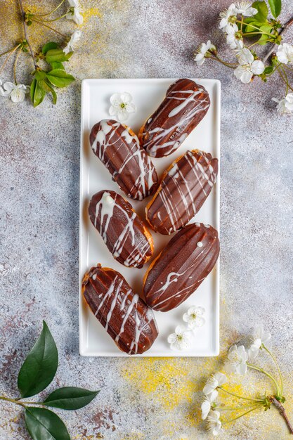 Eclairs ou profiteroles au chocolat noir et chocolat blanc avec de la crème anglaise à l'intérieur, dessert français traditionnel.vue d'en haut.