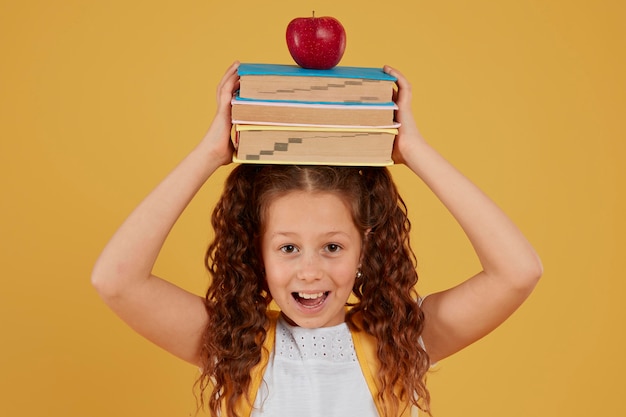 Photo gratuite Écolière tenant des livres et pomme sur sa tête