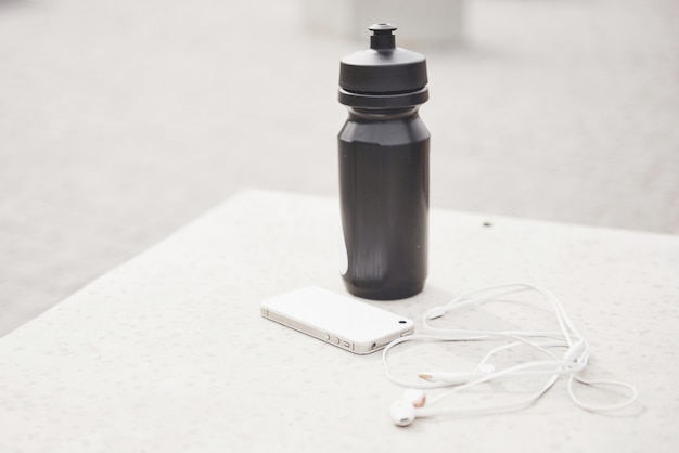 Des écouteurs de téléphone et une bouteille d'eau en plein air. Accessoires pour les sports de course