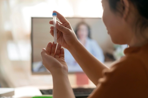 L'écouvillonnage nasal de la main d'une femme asiatique teste par elle-même des tests rapides pour la détection du virus co2 du SRAS par l'instruction télé-vidéo d'un médecin à la maison isole le concept de quarantaine