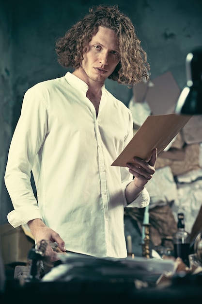 Photo gratuite Écrivain au travail. beau jeune écrivain debout près de la table et inventant quelque chose dans son esprit