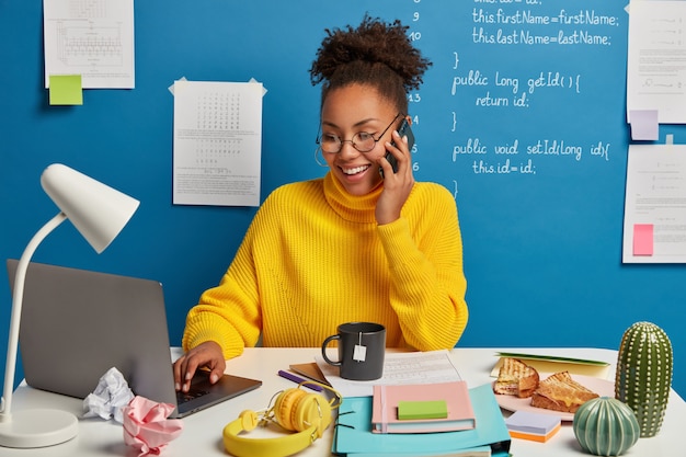 Un éditeur Web Professionnel Crée La Structure Technique Du Site Web, Discute De Certains Problèmes De Travail Via Un Smartphone, Porte Des Lunettes, Surfe Sur Internet Sur Un Ordinateur Portable Moderne.