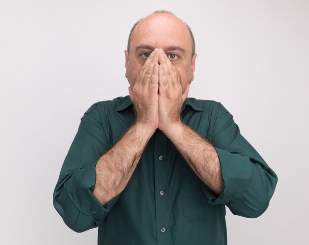 Effrayé homme d'âge moyen portant un t-shirt vert visage couvert avec les mains isolé sur mur blanc