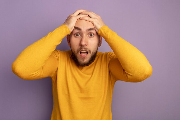 Effrayé jeune beau mec a attrapé la tête isolée sur le mur violet