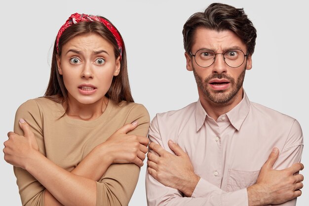 Effrayé jeune couple posant contre le mur blanc