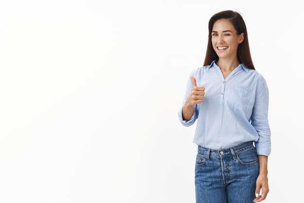 Effronté confiant femme d'affaires objectif succès gagner accord clin d'œil impertinent souriant heureux montrer pouce vers le haut geste sourire jugement positif comme votre idée se tenir debout fond blanc donner son approbation