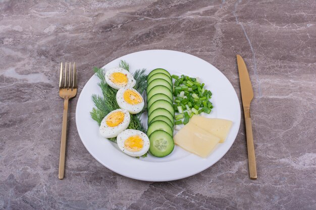 eggsufs durs avec des tranches de concombres et d'herbes dans une assiette blanche.